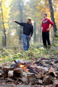 Campfire in forest with young people in background